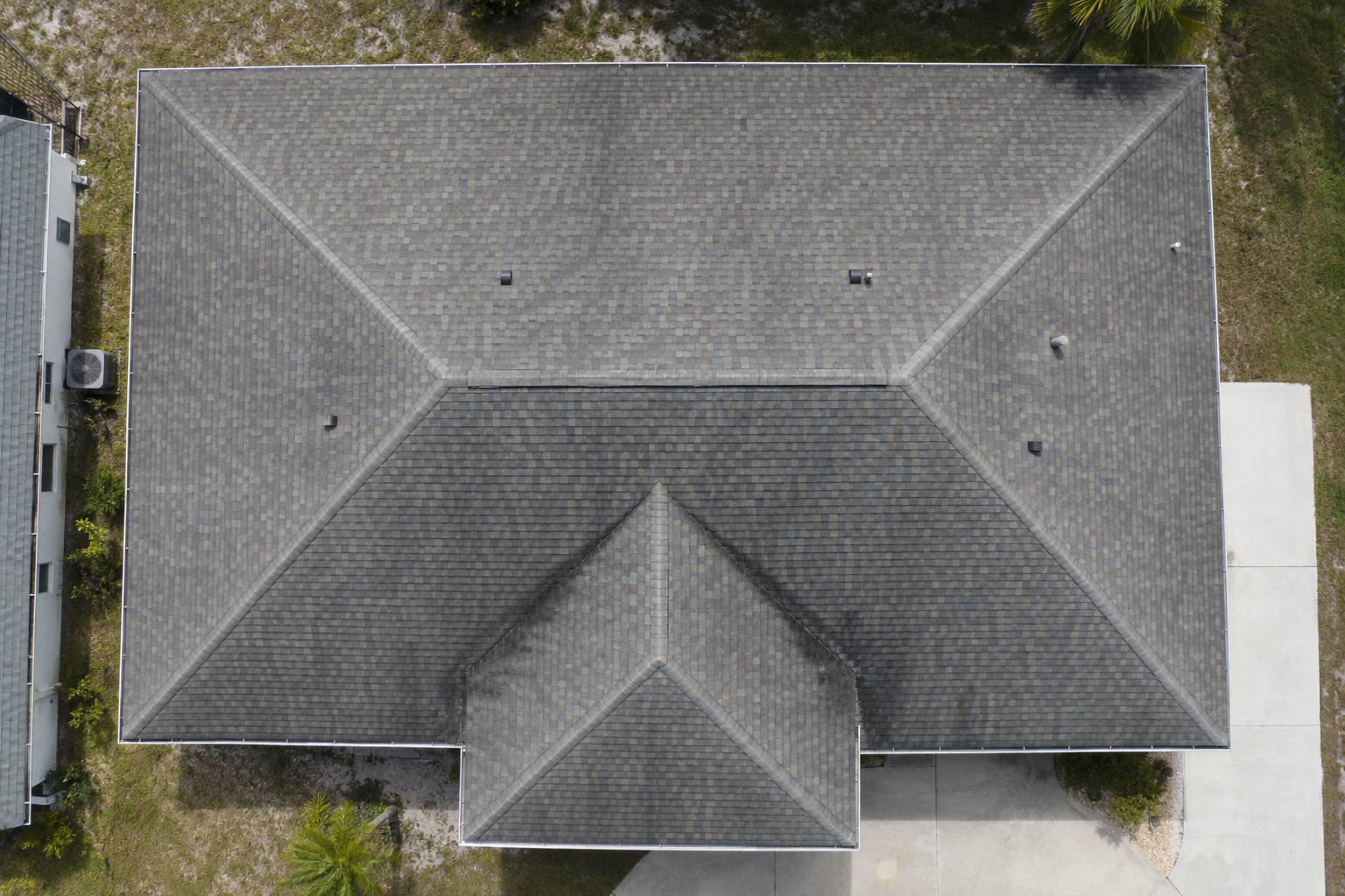 Drone's-eye view of a shingle hip roof with worn valleys